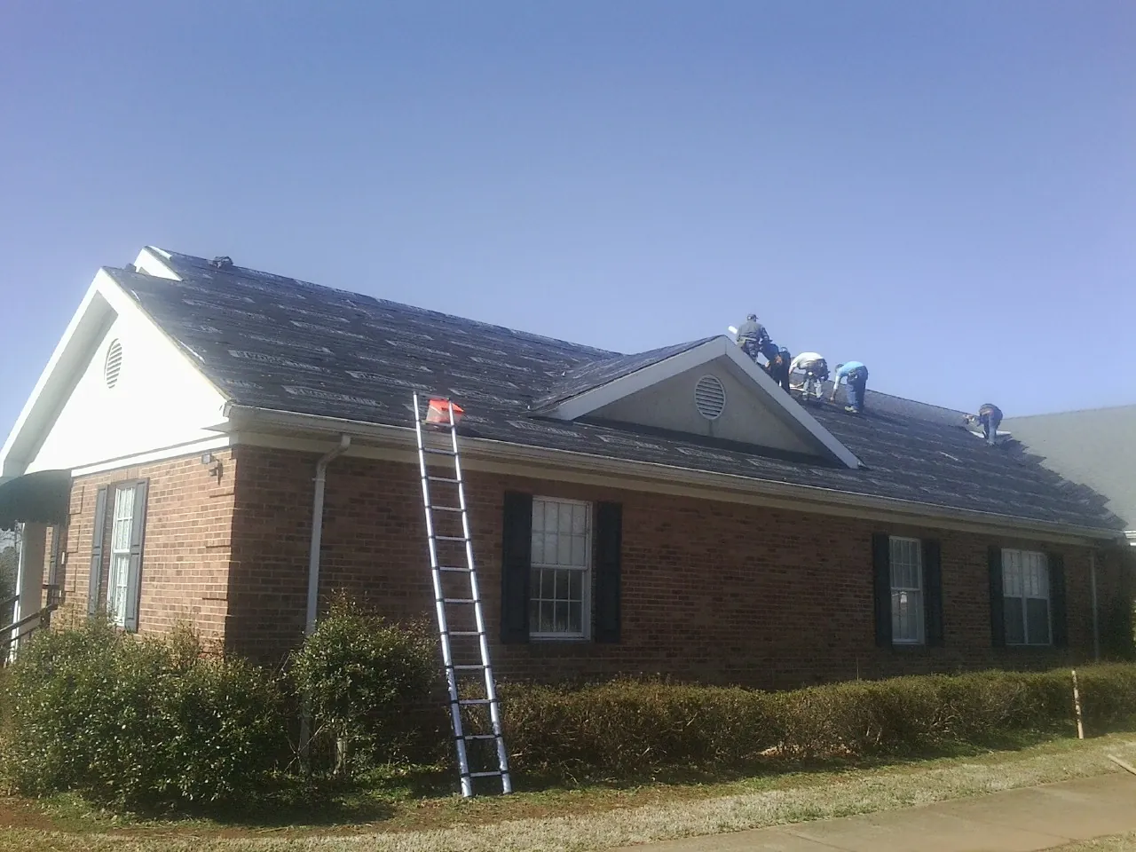 Crew tearing shingles off a brick ranch roof with a ladder set — Emergency Roof Repair work by our crew in Crete