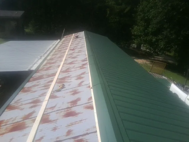 Old rusted panels beside newly installed green metal roofing — Wind Damage Roof Repair by Roofing Brothers in Crete