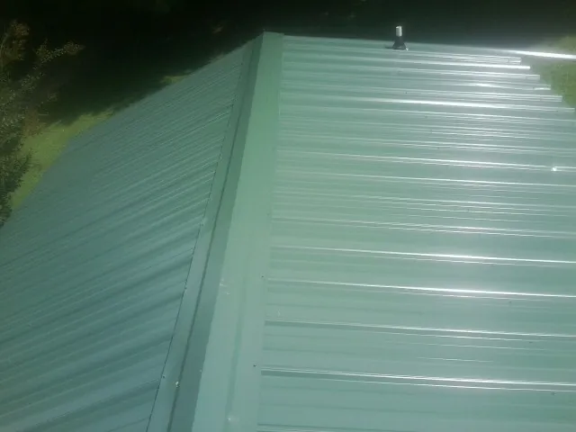 New green metal panels meeting at the ridge of a roof — Flat Roof Repair work by our crew in Crete