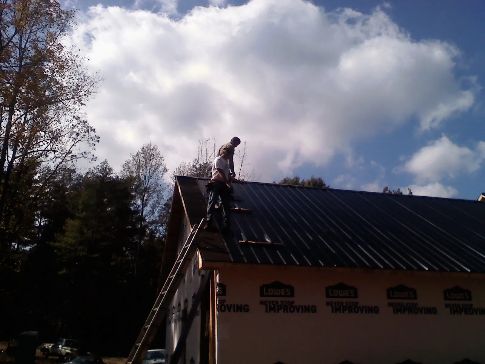 Roofer fastening dark metal panels high against a cloudy sky, from a Roof Inspection job in Crete