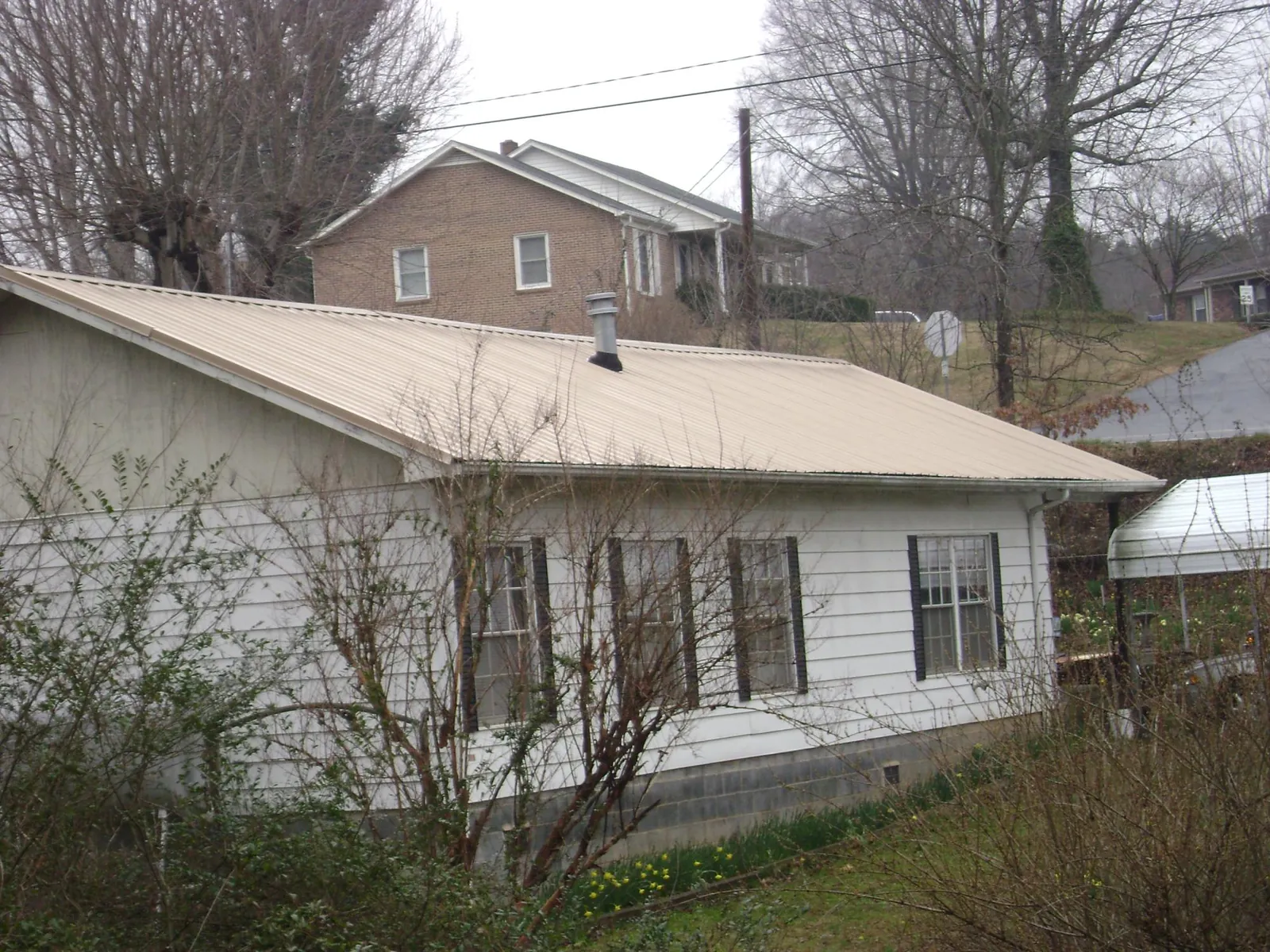 Tan metal roof on a white sided house set into a hillside — Commercial Roofing by Roofing Brothers in Crete